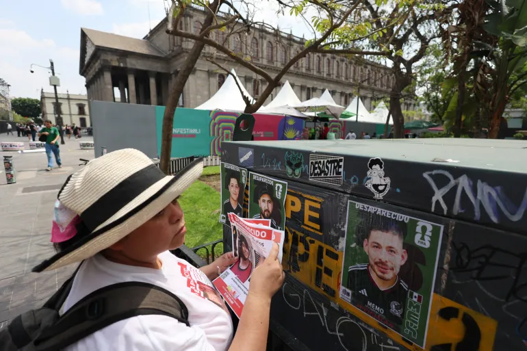 Colectivo Luz de Esperanza de Jalisco Collective-এর একজন সদস্য নিখোঁজ-ব্যক্তির ফ্লায়ারগুলিকে আটকানো চিহ্নের কাছে ধারণ করেছেন যাতে নিখোঁজ থাকা তাদের প্রিয়জনদের ছবি রয়েছে, যা 