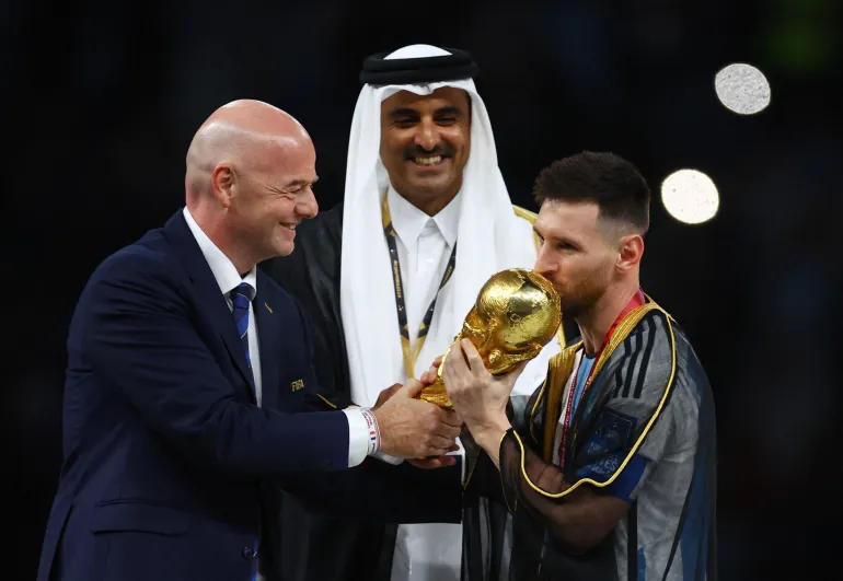 সকার ফুটবল - ফিফা বিশ্বকাপ কাতার 2022 - ফাইনাল - আর্জেন্টিনা বনাম ফ্রান্স - লুসাইল স্টেডিয়াম, লুসাইল, কাতার - 18 ডিসেম্বর, 2022 আর্জেন্টিনার লিওনেল মেসি ট্রফিটি চুম্বন করছেন যখন তাকে ফিফা সভাপতি জিয়ান্নি ইনফ্যান্টিনো কাতারের আমির আল তাবিন হাবিন শেখের সাথে এটি উপহার দিচ্ছেন ফাফেনবাখ
